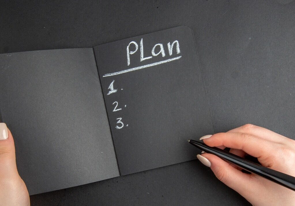 top view black notebook and pen in female hand on black background